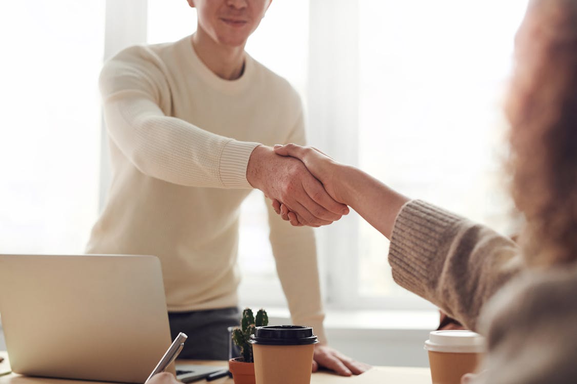 A real estate agent warmly guides a client through the entryway of a bright, modern home, illustrating the rewarding outcome of getting a real estate license.
