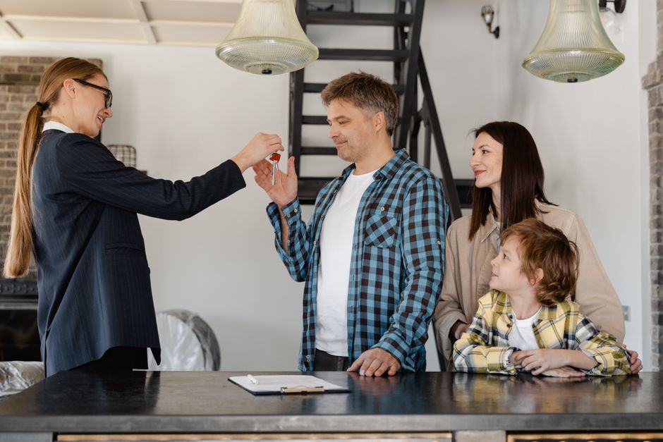 A real estate agent hands the keys to a modern home to a smiling couple, representing the enhanced, seamless client service offered by a dually-licensed professional.